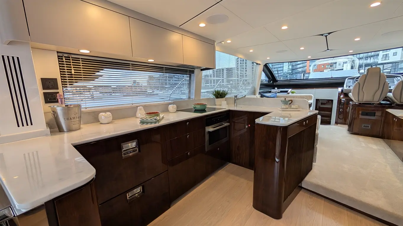 Modern yacht kitchen with dark wood cabinetry, marble countertops, kitchen appliances, and a view through large windows.